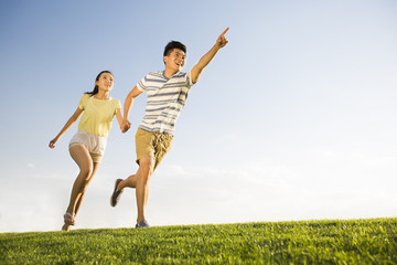 Fototapeta na wymiar Cheerful young couple holding hands running on grass