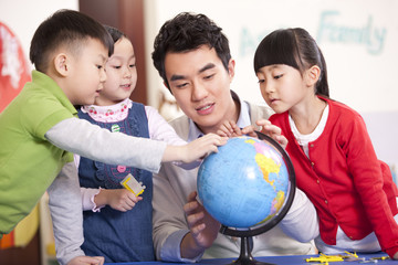 Male teacher teaching kindergarten children using globe