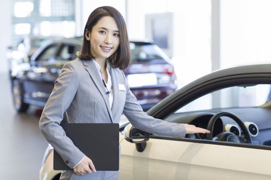 Confident saleswoman standing with new cars in showroom