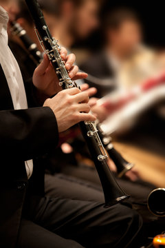Hands of man playing the clarinet in the orchestra in dark colors