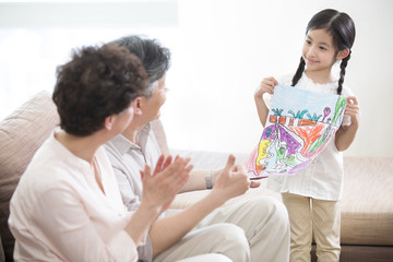 Obraz na płótnie Canvas Cute girl showing drawing to grandparents