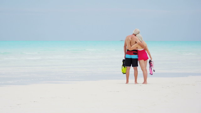 Caucasian senior travellers in swimwear on a beach with snorkels