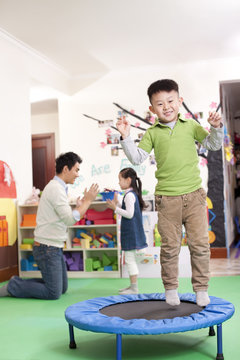 Happy boy jumping on a small trampoline with teacher and classmate in background
