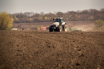 tractor on big wheels cultivates raises dust on ploughed soil