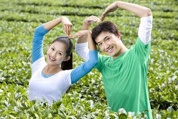 Fototapeta na wymiar Young Couple in Tea Field Making Heart Shapes with their Arms