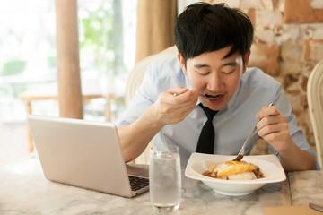 Fototapeta na wymiar Young Asian man working while eating with his laptop in restaurant
