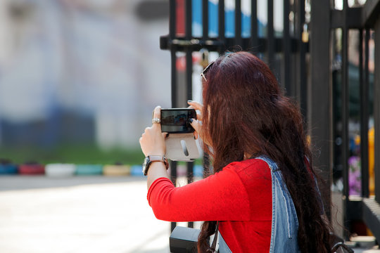 red hair young woman taking photo of beautiful wall with smart phone.