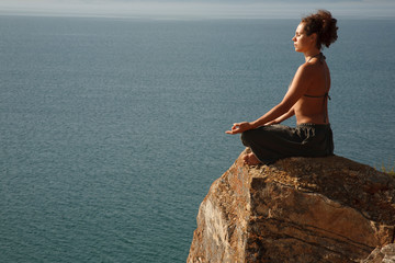 Real yoga instructor practicing on the rock near water line