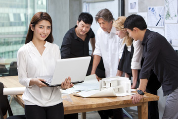  Architect holding laptop in studio with her team in background