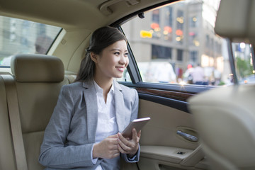 Businesswoman holding smart phone in car back seat