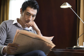 Naklejka premium Young businessman reading newspaper in study