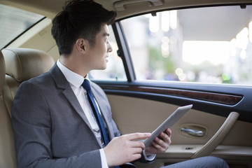 Businessman using digital tablet in car back seat