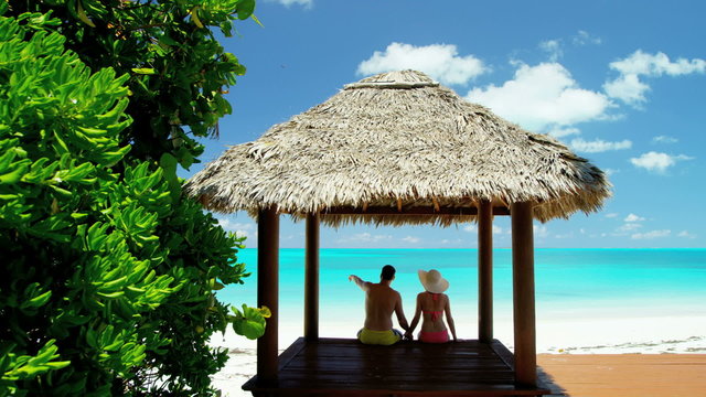 Caucasian couple sitting in a Caribbean tiki hut