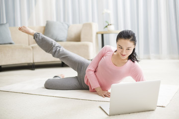 Young woman practicing yoga with laptop in living room