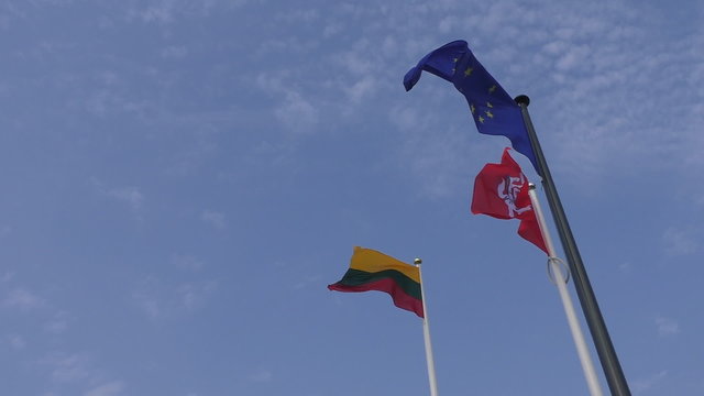 Three flags on the poles waving against blue sky. Tricolour national flag of Lithuania, red color  historical variant state flag with Vytis, the Rider and blue flag of European Union with star circle