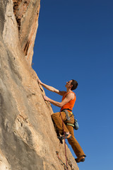 Young male climber hanging by a cliff.