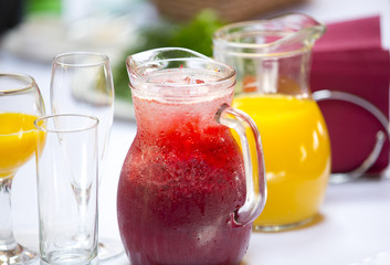 Fototapeta na wymiar Два кувшина с красным и желтым безалкогольными напитками со льдом на праздничном столе