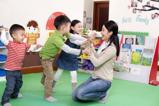 Happy kindergarten children playing clapping game with teacher