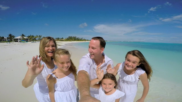 Video selfie of smiling Caucasian family playing barefoot on beach 