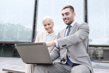 smiling businesspeople with laptop outdoors