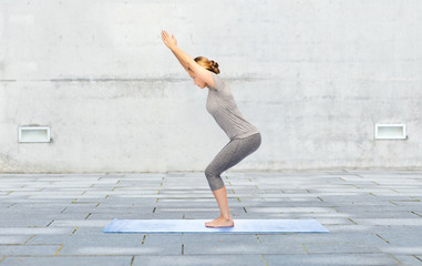 woman making yoga in chair pose on mat outdoors