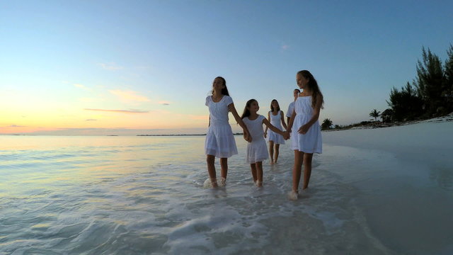 Caucasian family wearing white clothes barefoot on beach at sunset