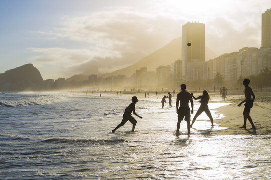 Beach football altinho silhouettes playing in the waves on the shore of Copacabana Beach at sunset in Rio de Janeiro, Brazil 