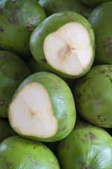 Pile of fresh green coconuts waiting to be opened for coconut water sit outdoors in tropical light