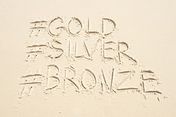 Hashtag social media message for gold, silver, and bronze medals, sport's first, second, and third place, written in sand on the beach in Rio de Janeiro, Brazil