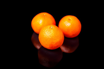 Three tangerines lie on a black mirror.