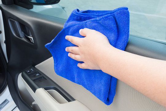 Woman hand cleaning interior car door panel with microfiber clot