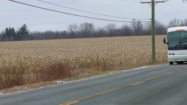 Coach (bus) passing a field of corn (maize).  Close view, colored for a cold, winter look.  Originally recorded in 4K, UHD.