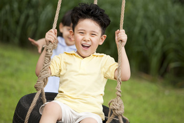 Excited boy playing on a swing with little girl behind