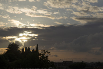 Naklejka premium Cityscape in Rome at dusk with sun behind the clouds. Silhouette of trees.