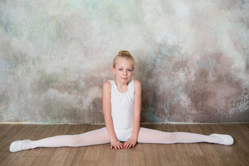 Little ballet dancer doing stretching before class in a white bathing suit, dance, sports, healthy...