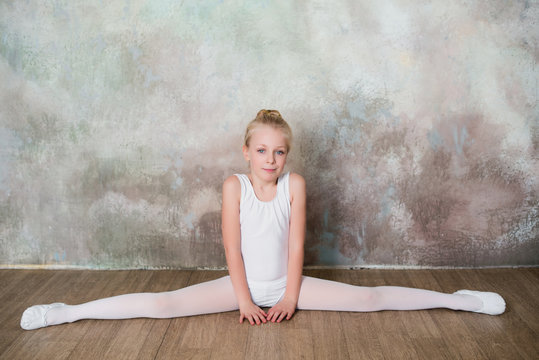 Little ballet dancer doing stretching before class in a white bathing suit, dance, sports, healthy lifestyle, ballet