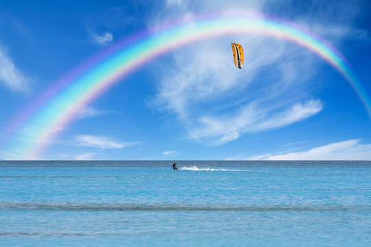 Kitesurfer in action on clear blue water under a rainbow