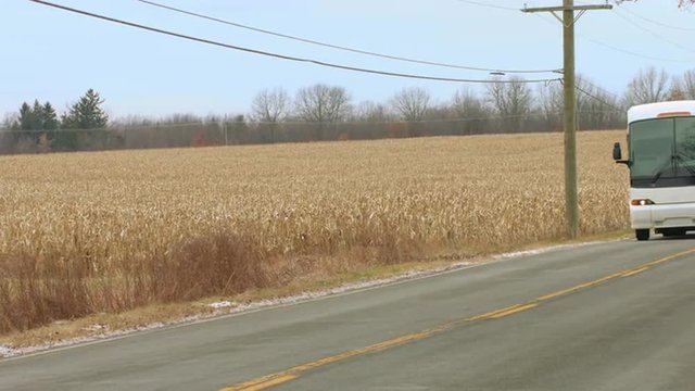 Coach (bus) passing a field of corn (maize).  Close view, colored for an autumn/fall look.  Originally recorded in 4K, UHD.