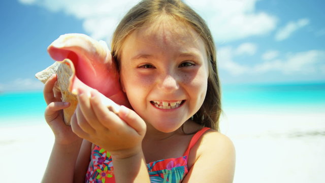 Portrait of cute young Caucasian girl on a beach vacation with a conch shell