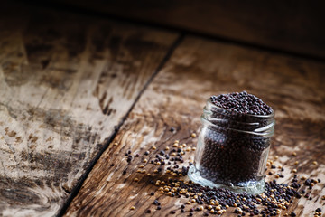 Black mustard seeds in a glass jar on the old wooden background,