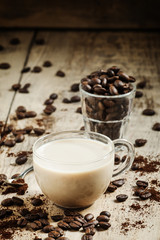 Glass cup of coffee with milk, spilled grain and ground coffee o