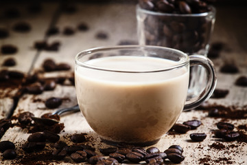 Glass cup of coffee with milk, spilled grain and ground coffee o
