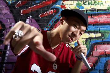 Teenage Boy Singing Into A Microphone In Front Of A Wall Of Graffiti