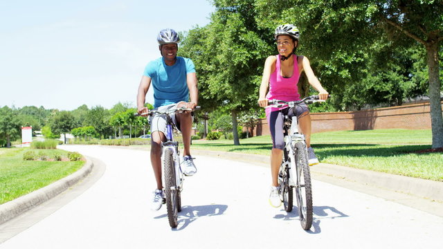 Young slim African American man and woman cycling outdoor