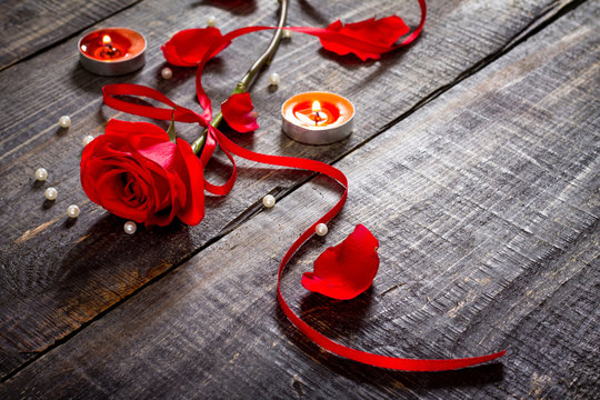 Red rose with red ribbon and candle on a dark background