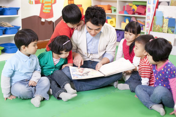 Male teacher reading picture book with cute kindergarten children