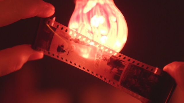 Photographer inspects negatives against red lamp in darkroom close-up