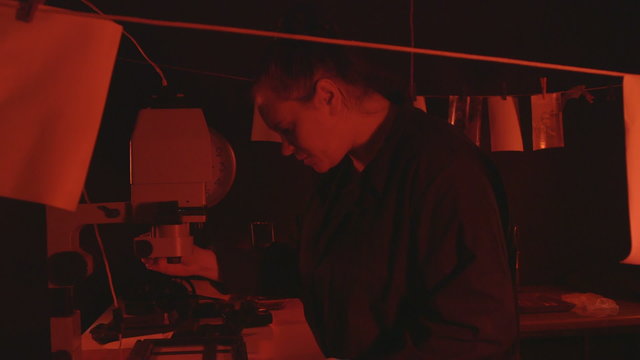Photographer using photographic enlarger to produce prints from film in darkroom