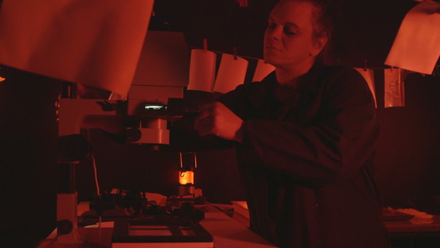 Woman photographer working in darkroom using enlarger to produce photographic prints