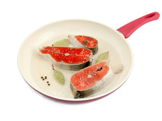 Salmon steaks in a frying pan with onions, bay leaves and flavourings on isolated background